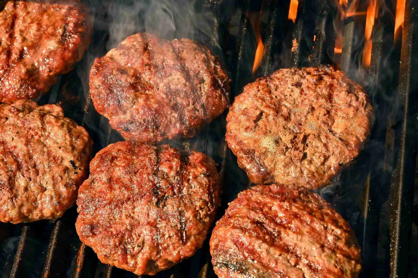 Grilled burger patties with char marks and rising smoke