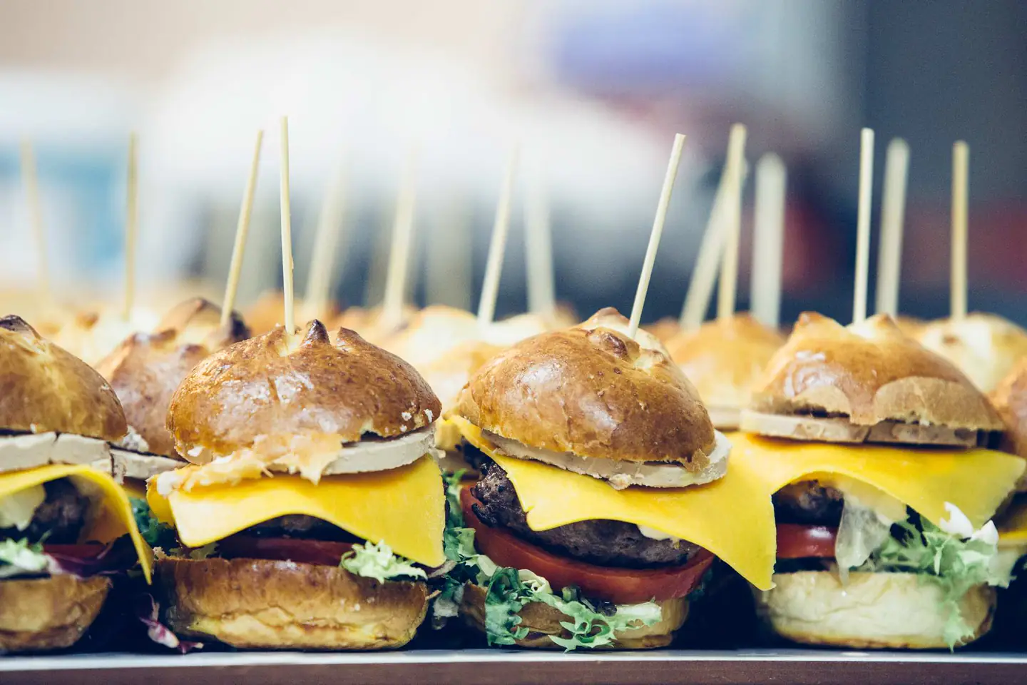 Row of slider burgers topped with cheddar cheese and lettuce