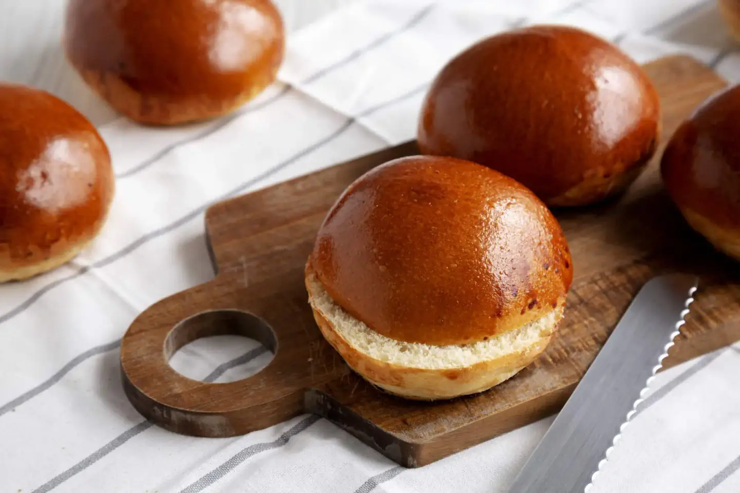 Glossy golden hamburger buns on a wooden cutting board