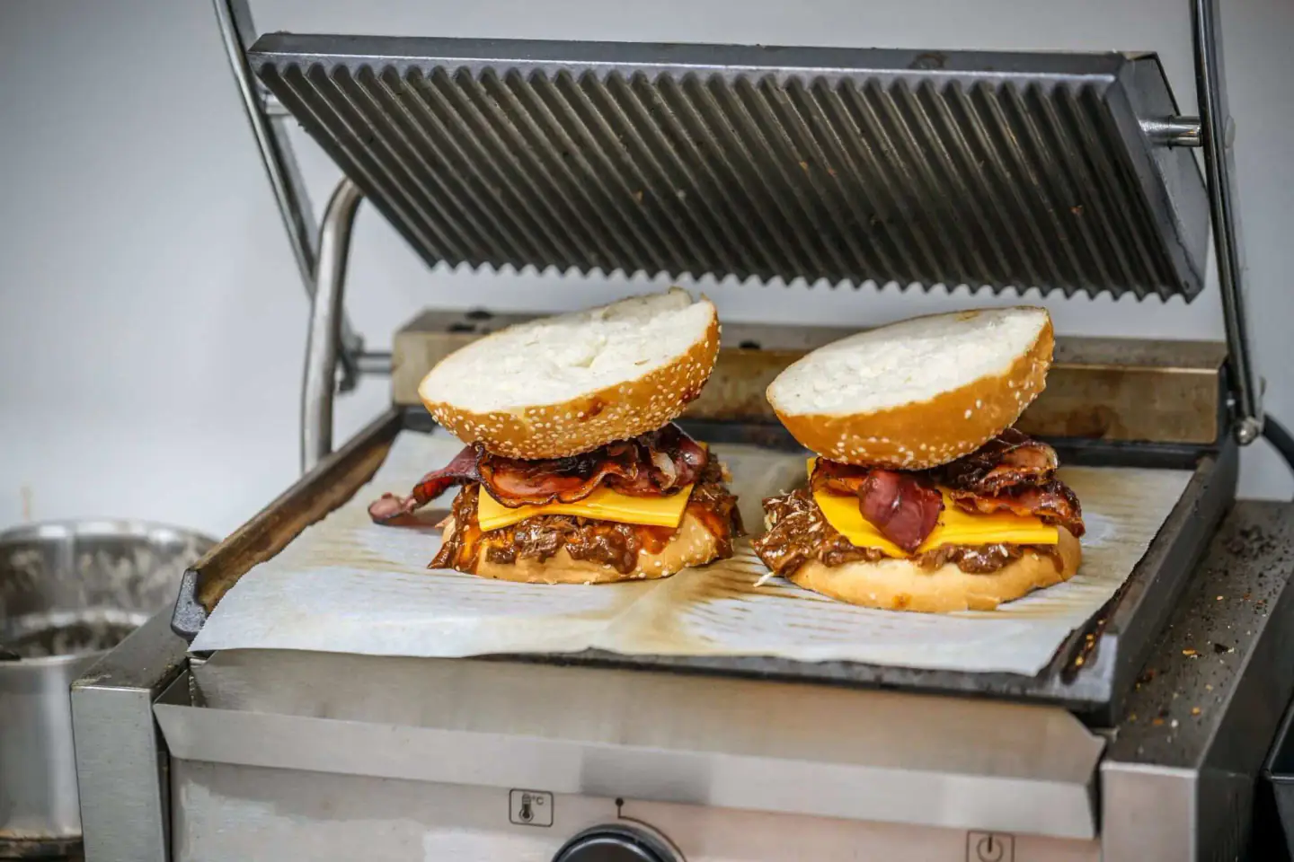 Two smashed bacon cheeseburgers with melted cheese being pressed on a griddle